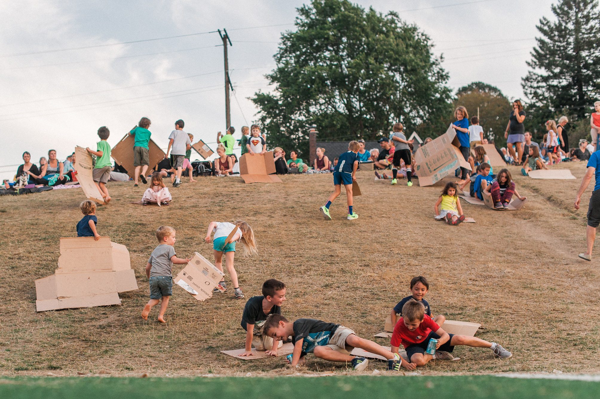 Local kids sliding down a grassy hill on pieces of cardboard while their parents wait for the Swifts to descend into Chapman Elementary School's Chimney. Photography by Briana Morrison