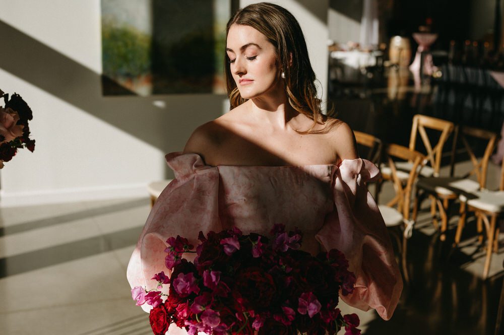 A styled bride in a pink wedding gown soaks up sun at the indoor ceremony site at Amaterra Wines. Photographed by Briana Morrison
