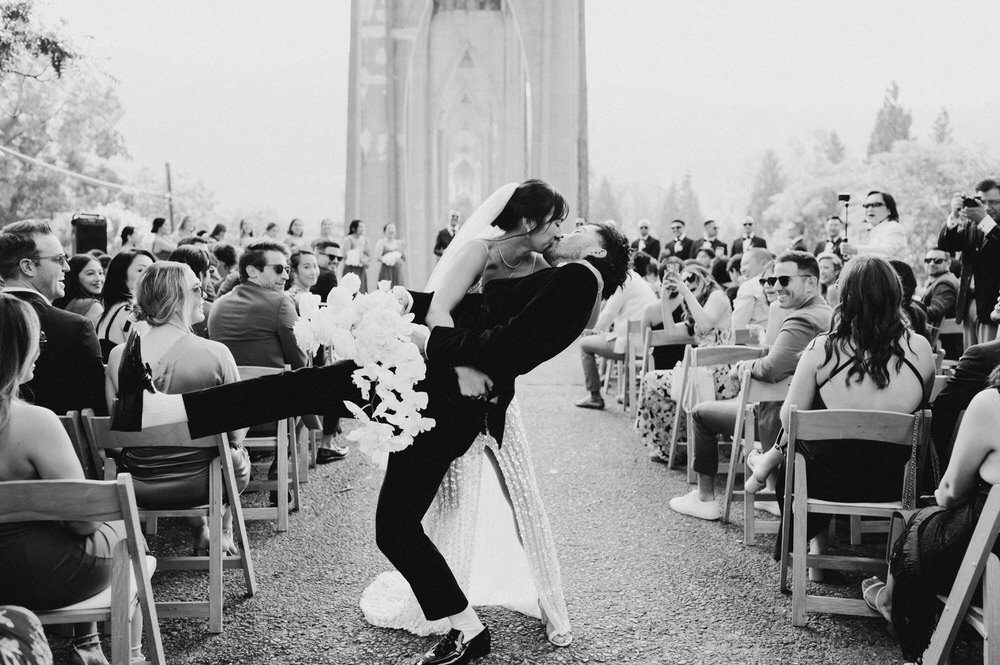 Oregon wedding photographer captures a black and white photograph of a bride dipping her groom in the aisle after the ceremony.