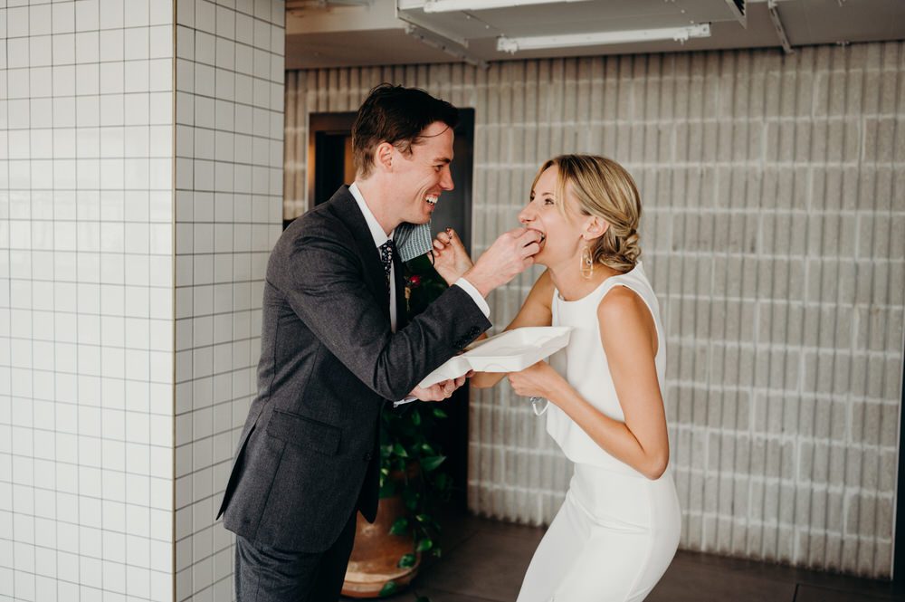 A bride and groom feed each other cake at their wedding while they laugh.