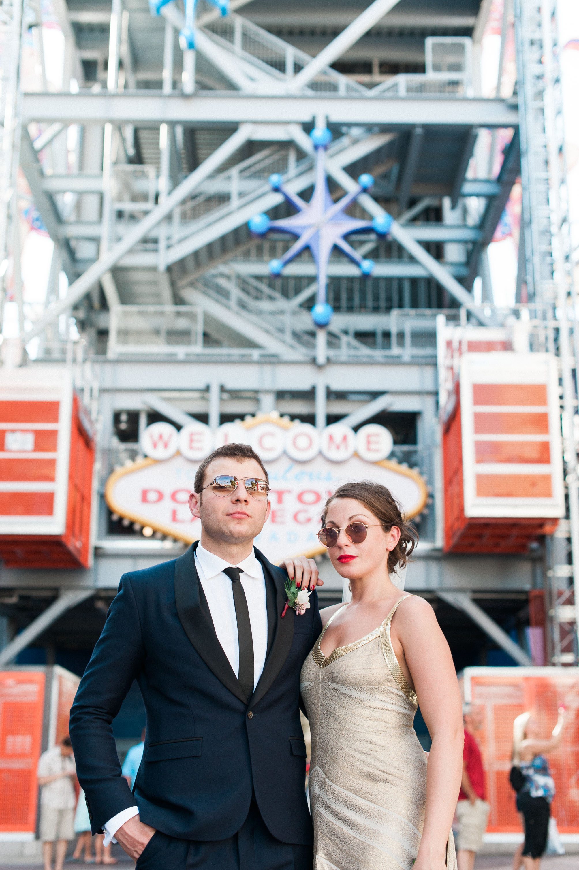 A badass bride in a gold dress and her groom standing in front of the Welcome to Downtown Las Vegas sign on Fremont Street. Captured by Las Vegas Elopement Photographer Briana Morrison