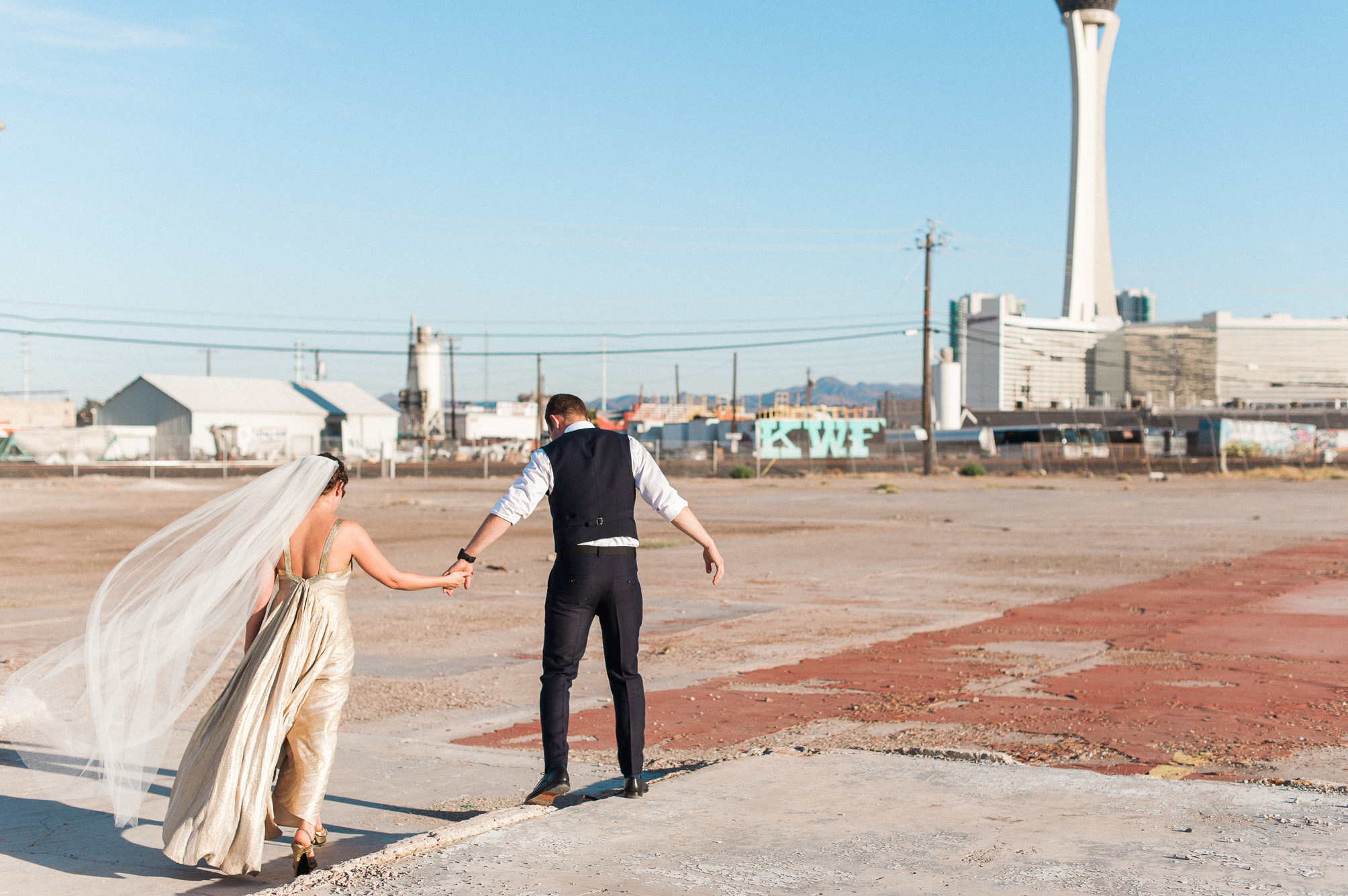 A beautiful bride in a gold dress walks with her groom in an abandoned lot in Las Vegas, Nevada. Photography by Las Vegas wedding photographer Briana Morrison