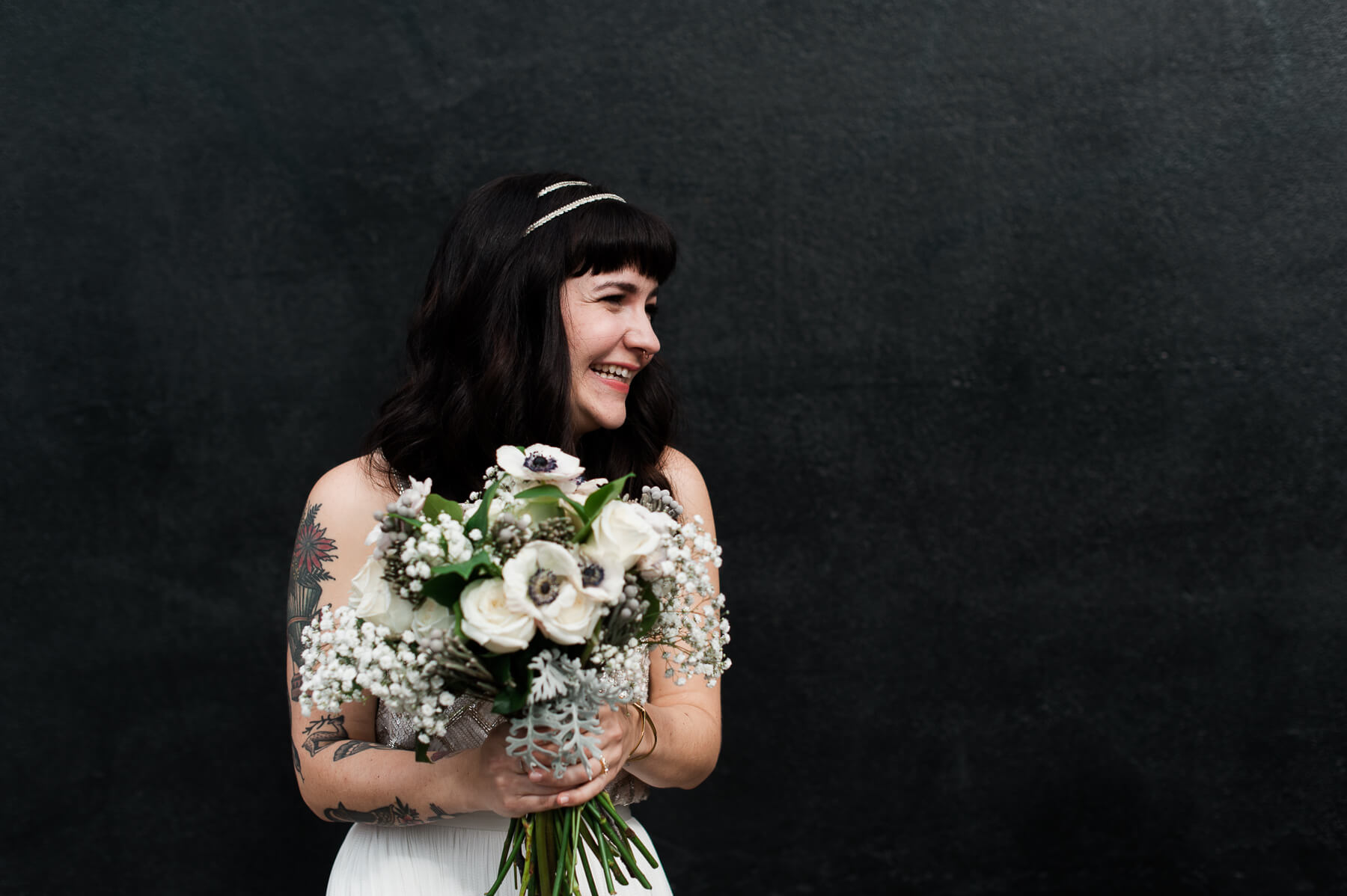 A very happy bride holding a beautiful bouquet in front of a black wall. By Portland Holocene Wedding Photographer Briana Morrison