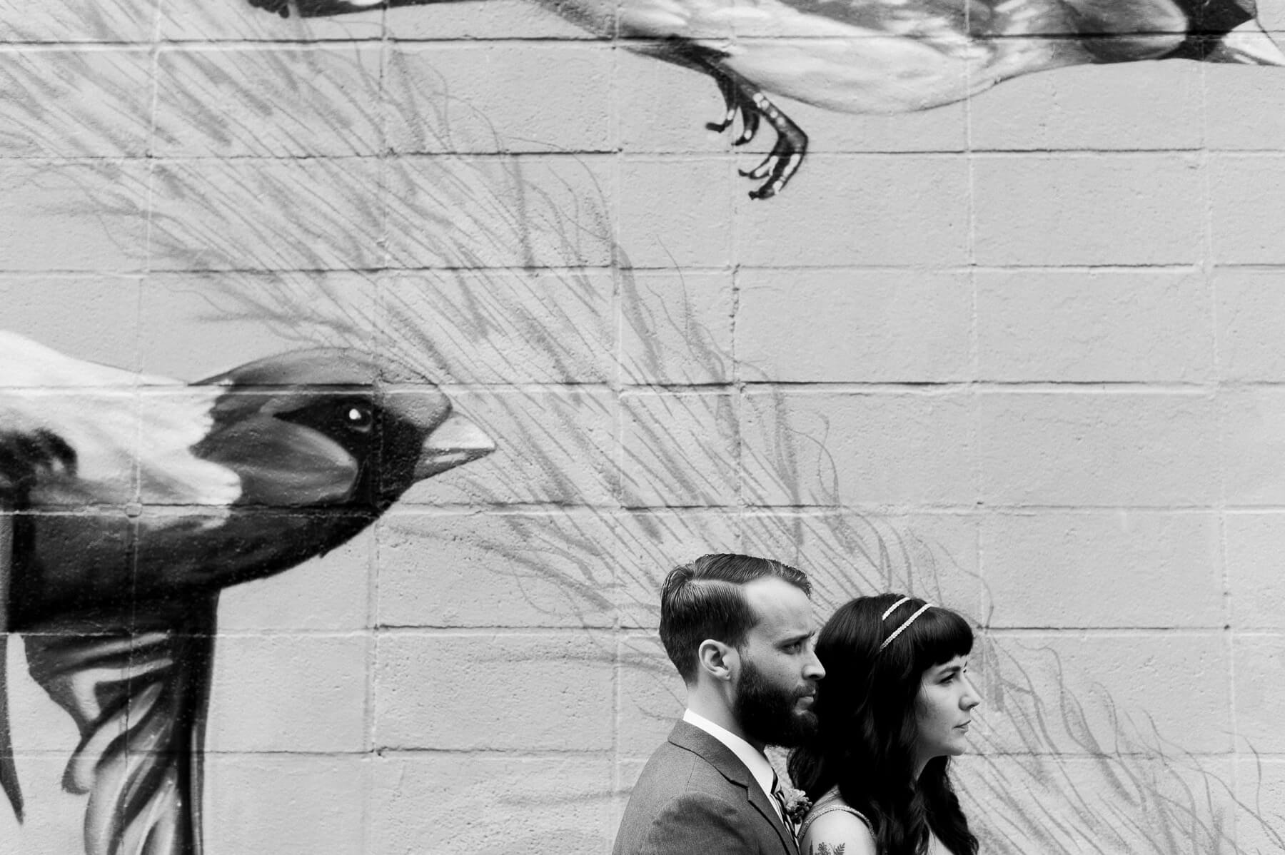 Black and white profile of a bride and groom in front of a bird mural in Portland, Oregon. By Portland Wedding Photographer Briana Morrison