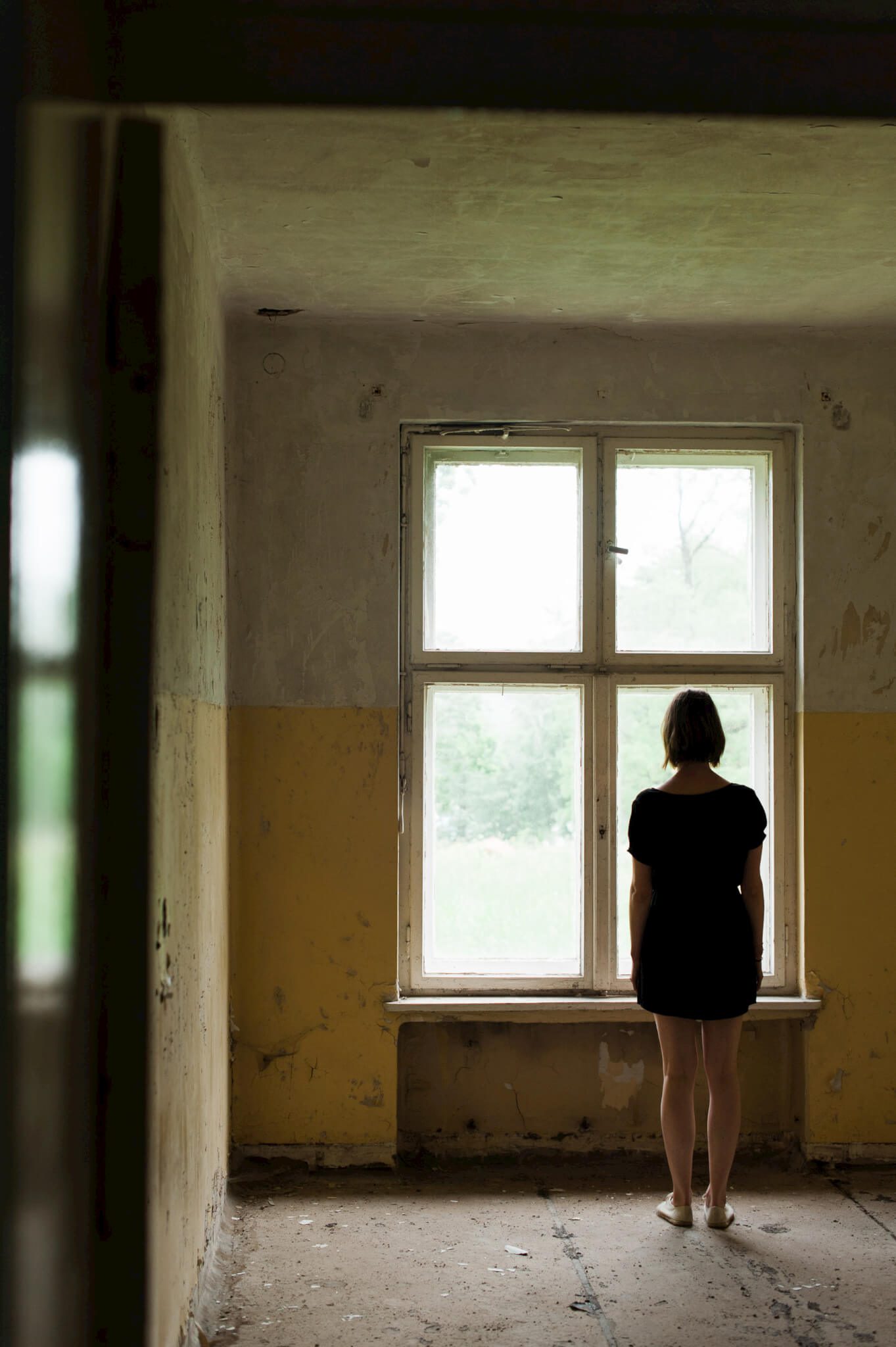 A woman looking out a window from inside the abandoned Heilstätten Hohenlychen Sanatorium in Lychen, Germany. Photographs by Berlin Portrait Photographer Briana Morrison