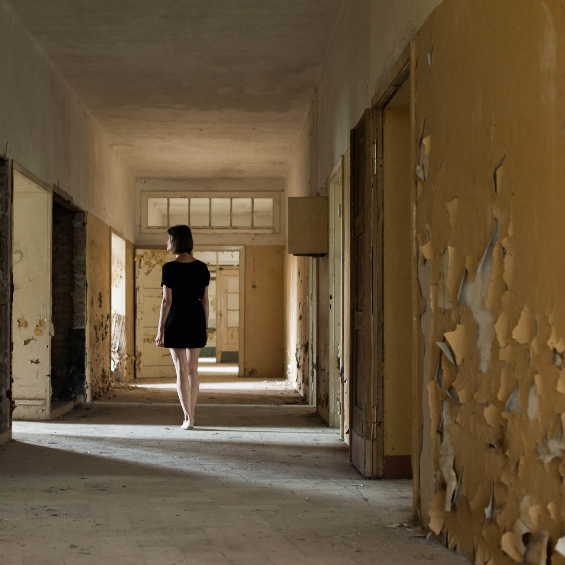 A woman looking through a doorway from inside the abandoned Heilstätten Hohenlychen Sanatorium in Lychen, Germany. Photographs by Berlin Portrait Photographer Briana Morrison