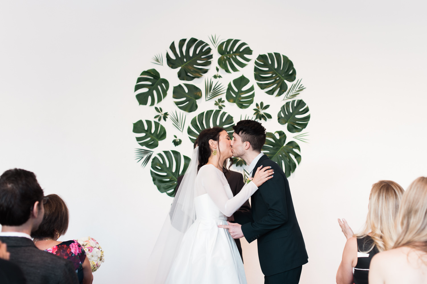 The kiss with a Monstera leaf backdrop. by Ace Hotel wedding photographer Briana Morrison
