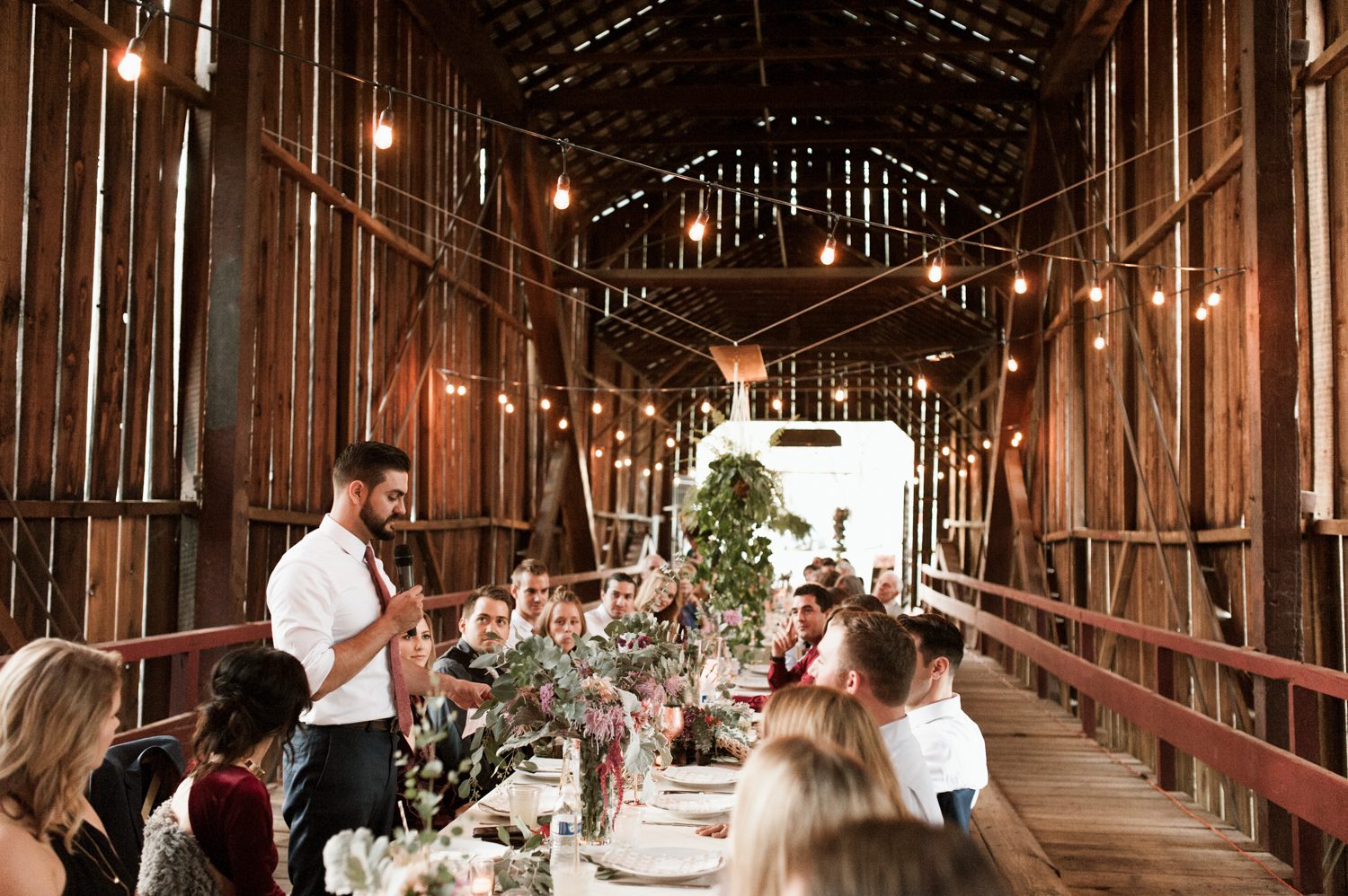The best man gives a toast to wedding guests in a covered bridge. By West Coast wedding photographer Briana Morrison