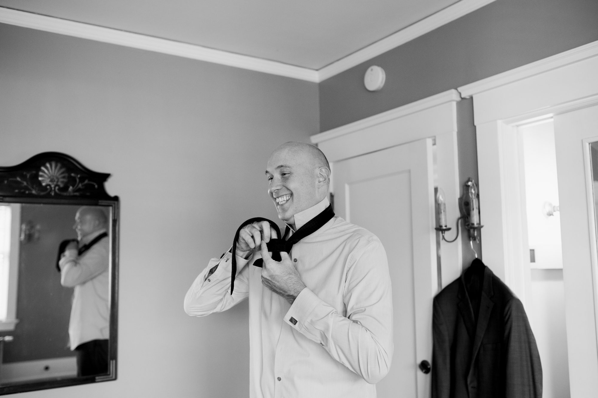 The groom puts on his tie in the Portland Mayor's Mansion. By Laurelhurst Park wedding photographer Briana Morrison