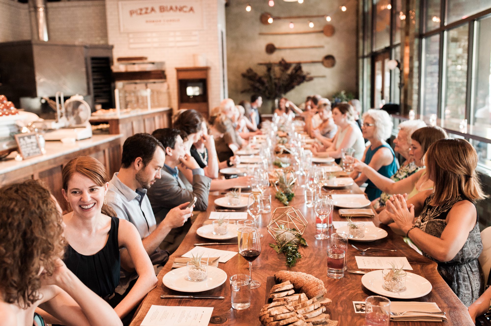Wedding guests sit down for dinner at Roman Candle Baking Co in Portland, Oregon. By wedding photographer Briana Morrison