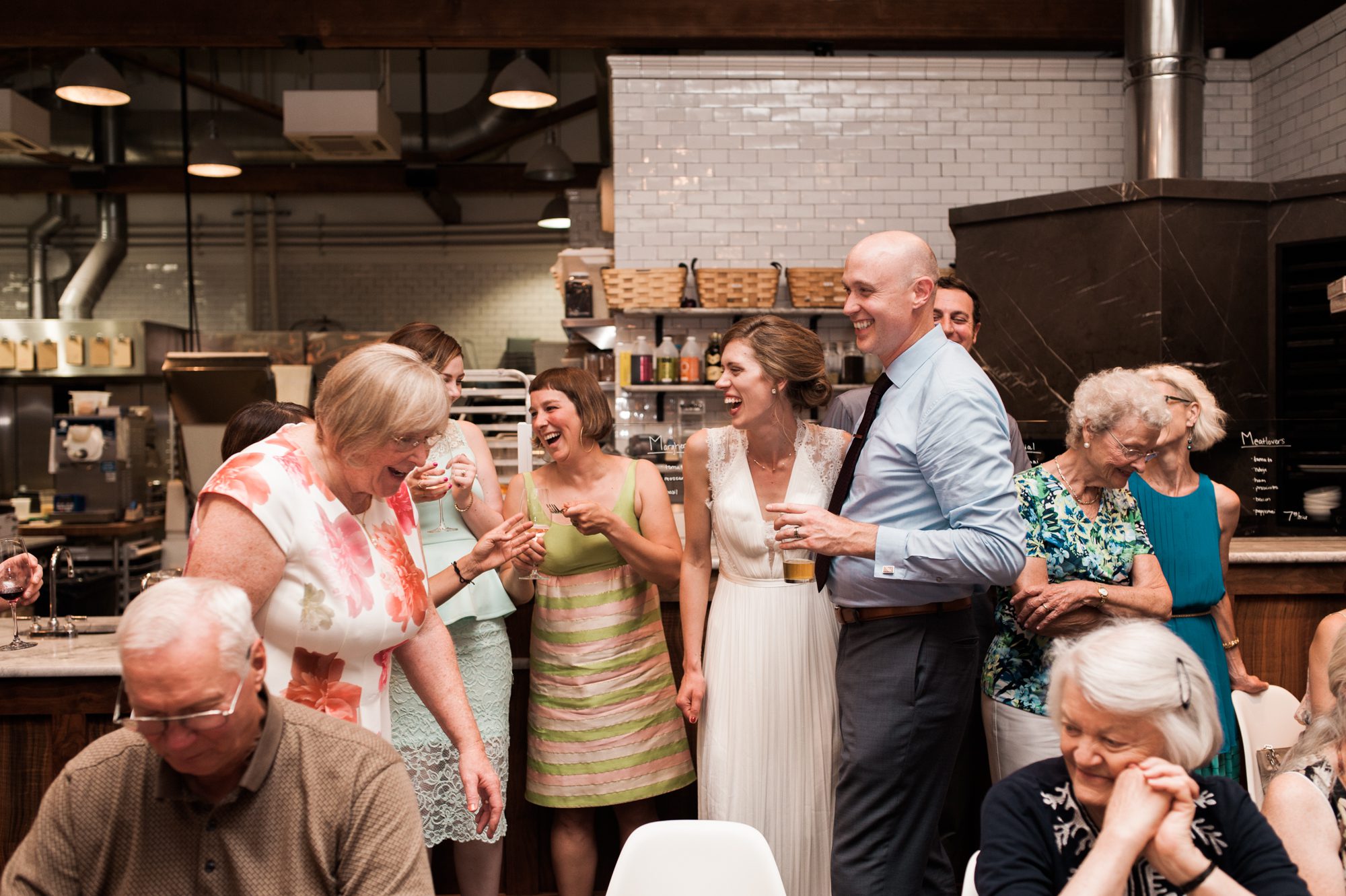 The bride and groom laugh with their wedding guests during their reception at Roman Candle Baking Co. By Laurelhurst Park wedding photographer Briana Morrison