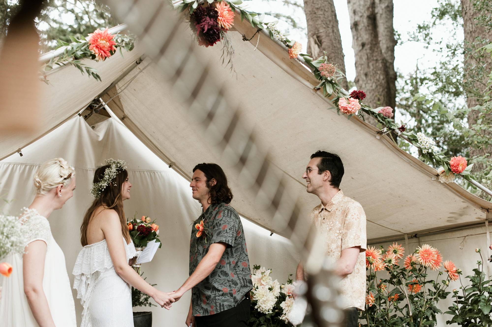 The bride and groom say their vows under a white tent decorated with flowers. By Long Beach, Washington wedding photographer Briana Morrison