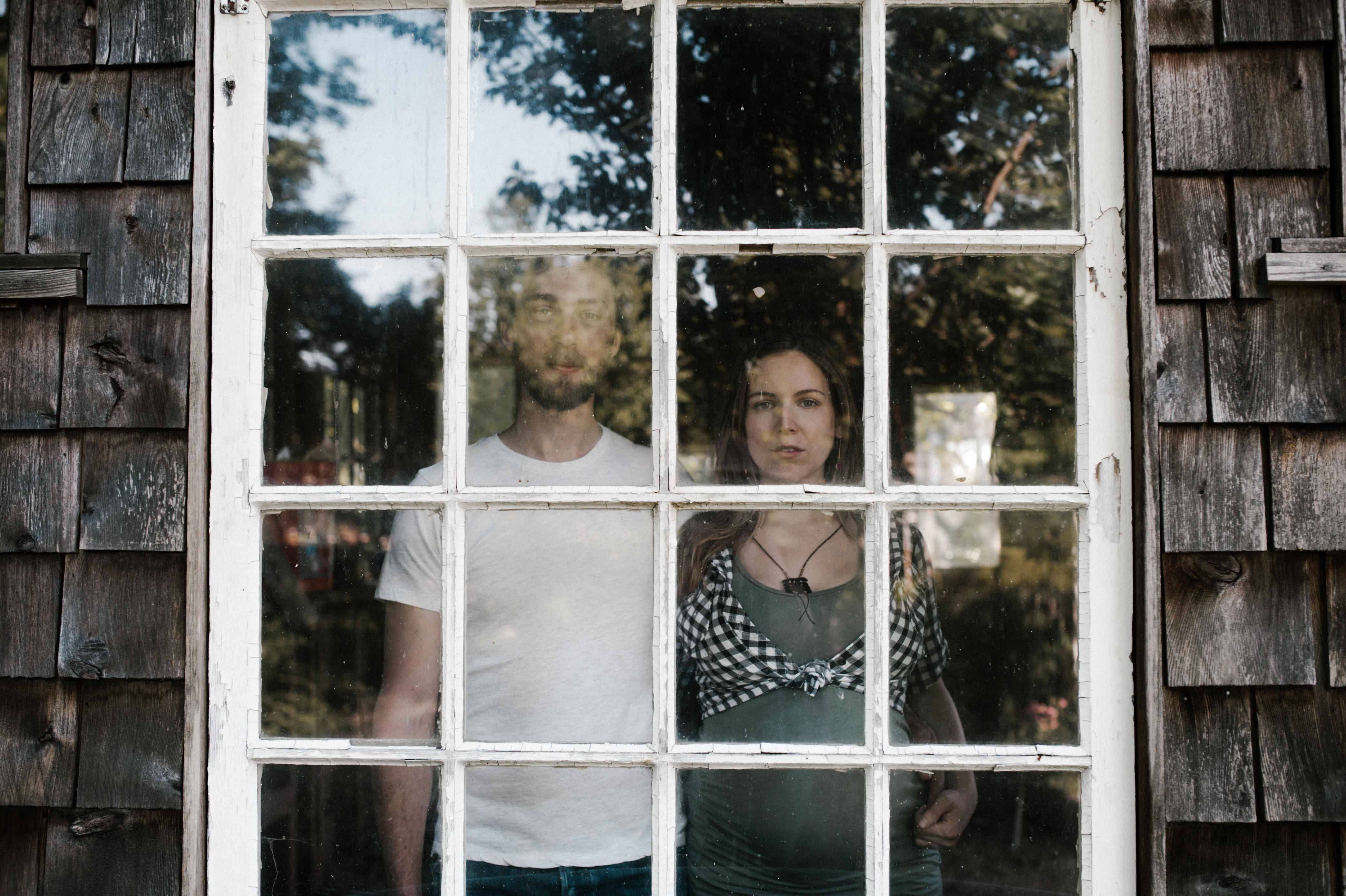 Portrait of a young couple standing behind a window. By Portland Maternity Photographer Briana Morrison