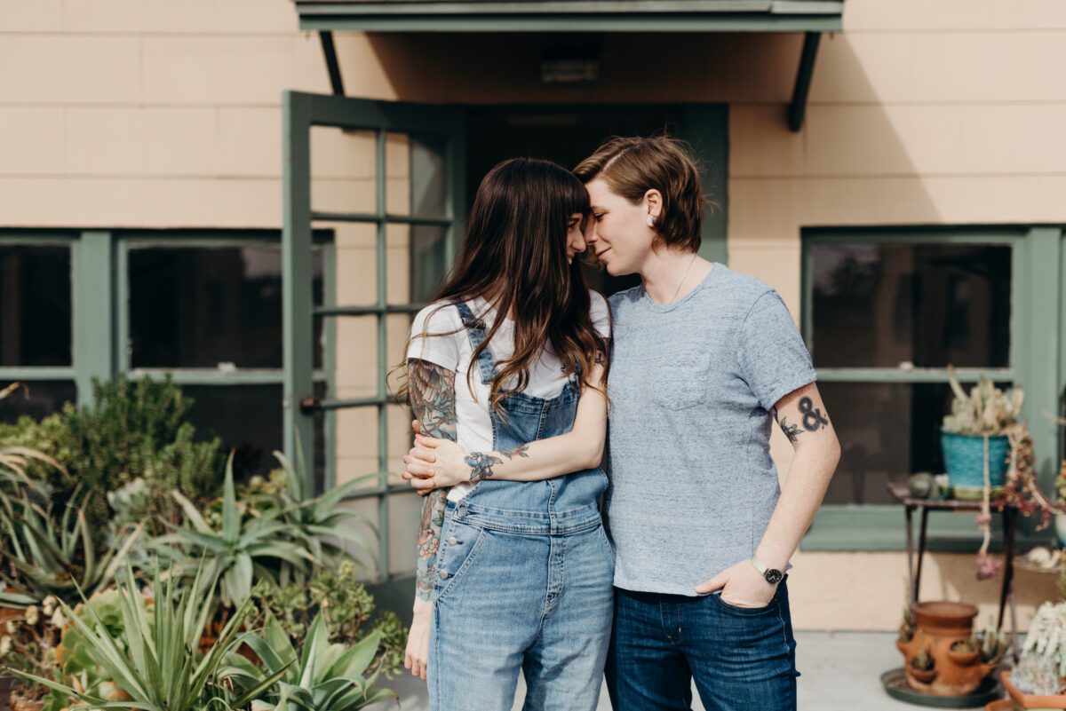 North Park San Diego engagement portrait of a same sex couple on their rooftop garden terrace standing side by side and nuzzling their faces together.