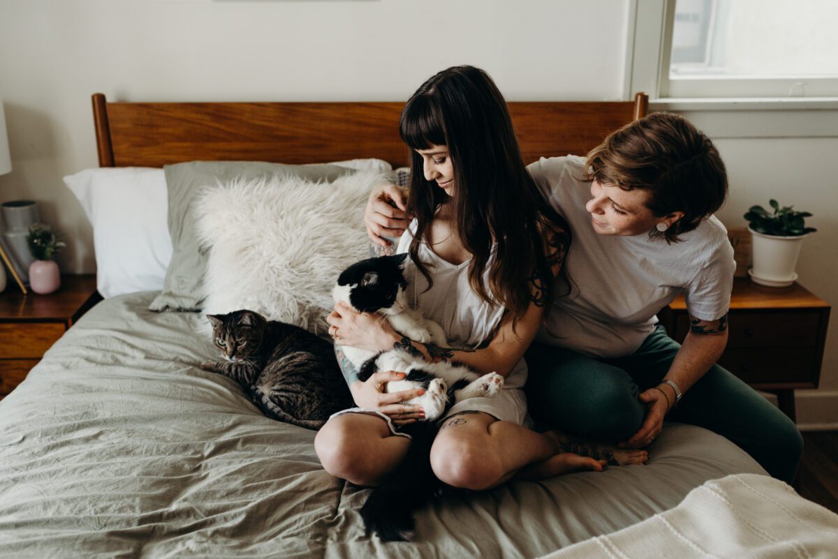 Cute photograph of a same sex couple sitting on their bed and snuggling with their cat.