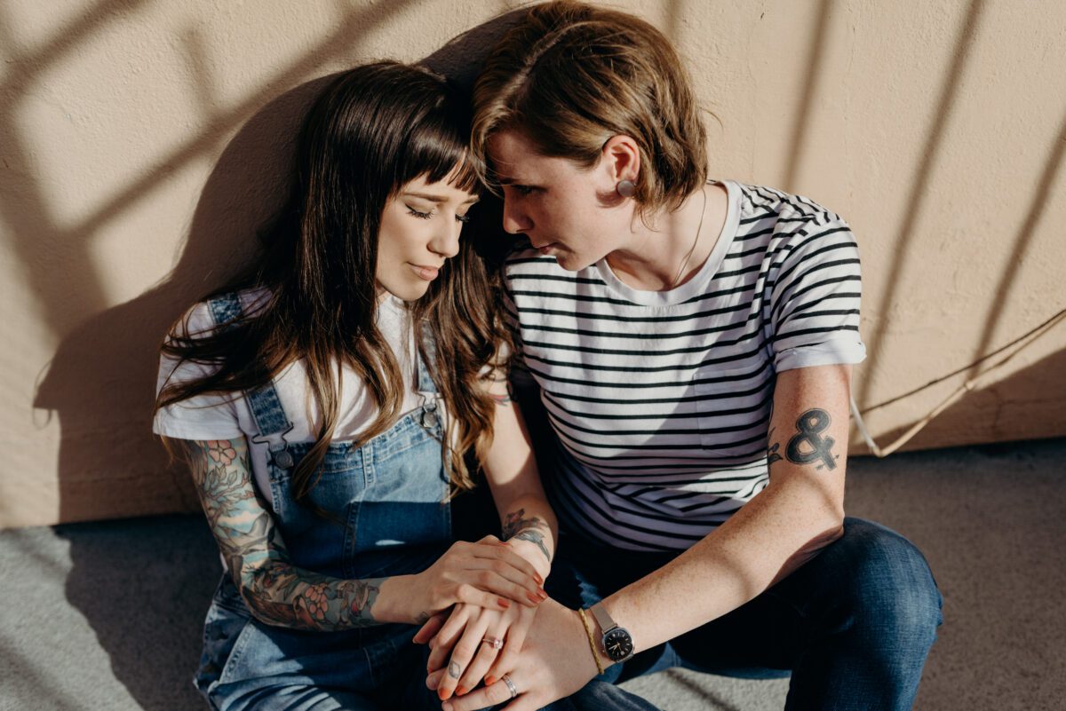 Same sex couple sits in the sunshine and cuddles during their engagement session on their rooftop terrace in San Diego.