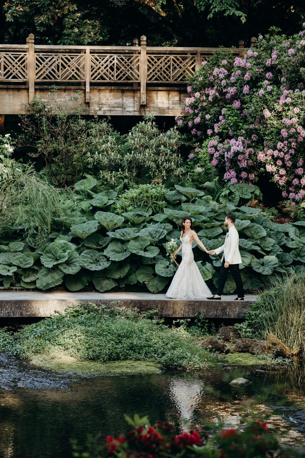 A bride and groom walk in the Crystal Springs Rhododendron Garden in Portland, Oregon. Photographed by Briana Morrison