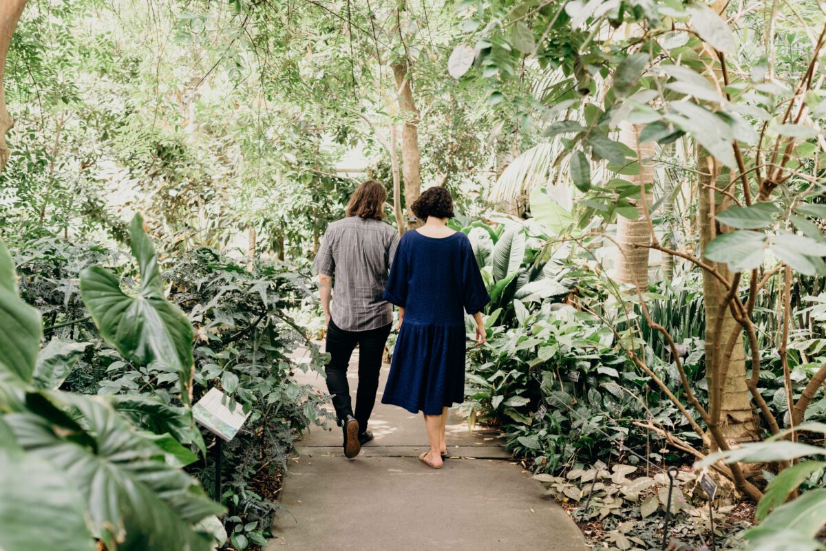 Brooklyn NY engagement portraits in Brooklyn Botanic Garden - a man and woman walk companionably through a lush garden.