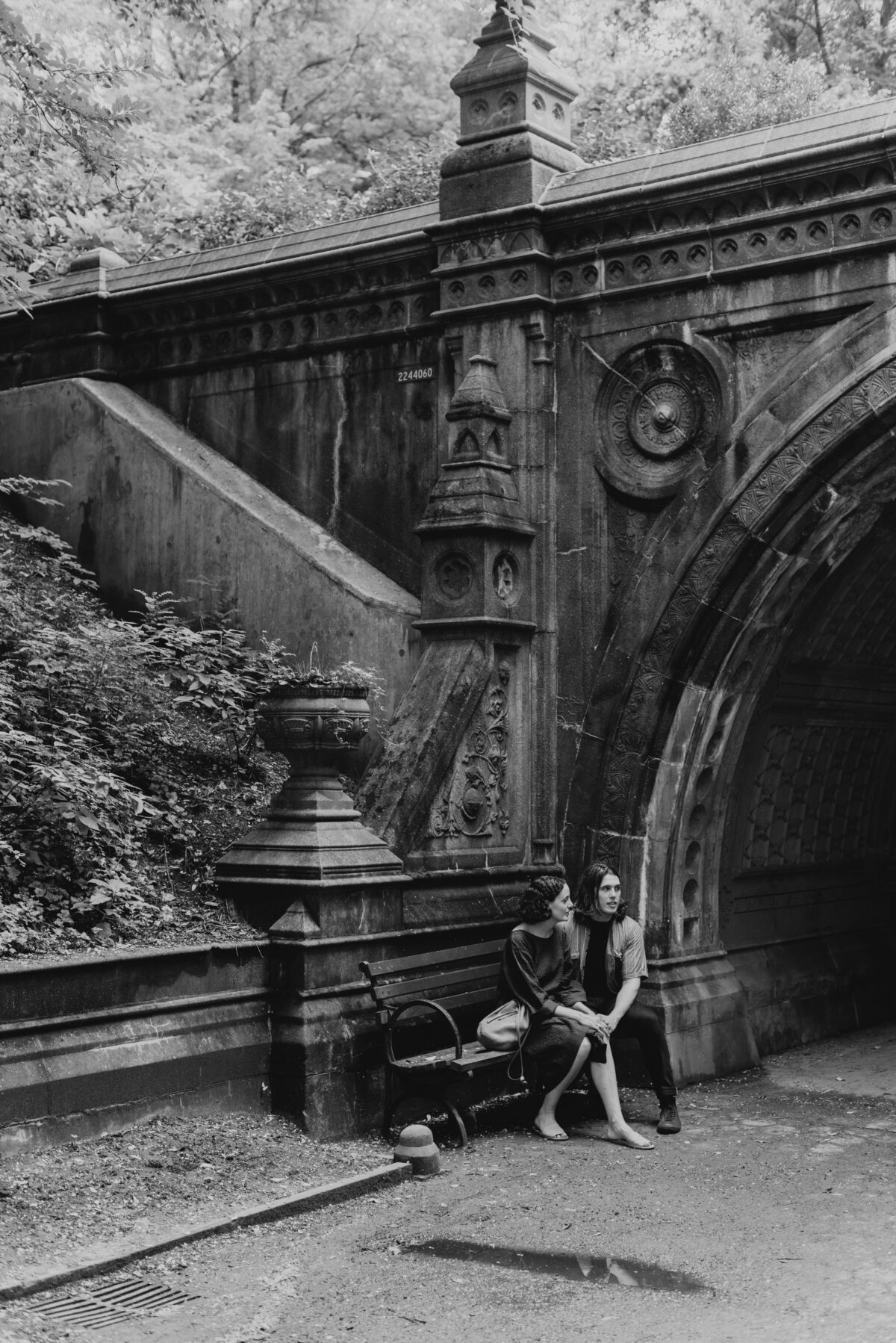 Black and white portrait of a young couple sitting under a bridge in Prospect Park.