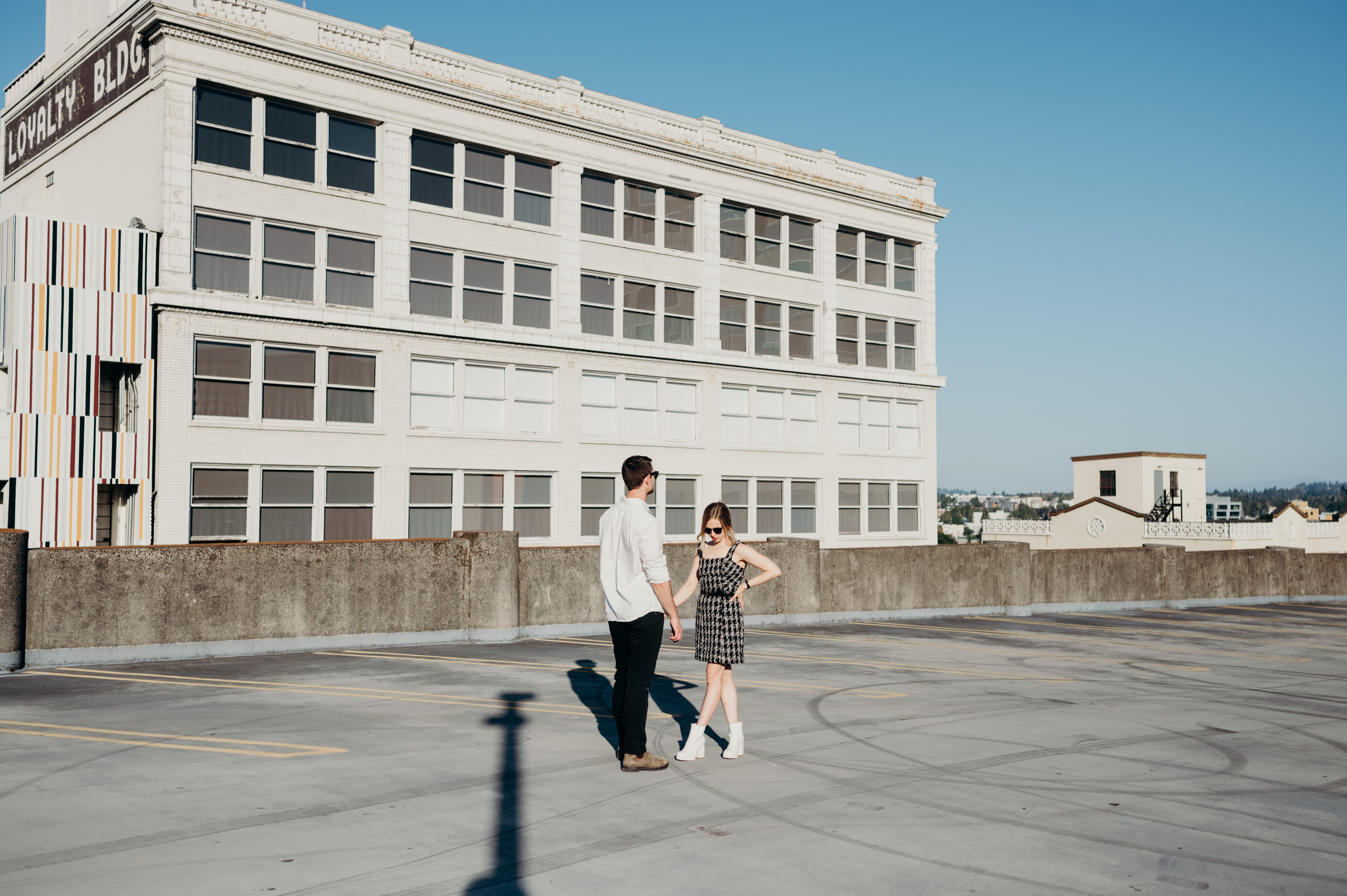 A man and woman stand in the sunshine on top of a parking garage for their Portland city view engagement session.