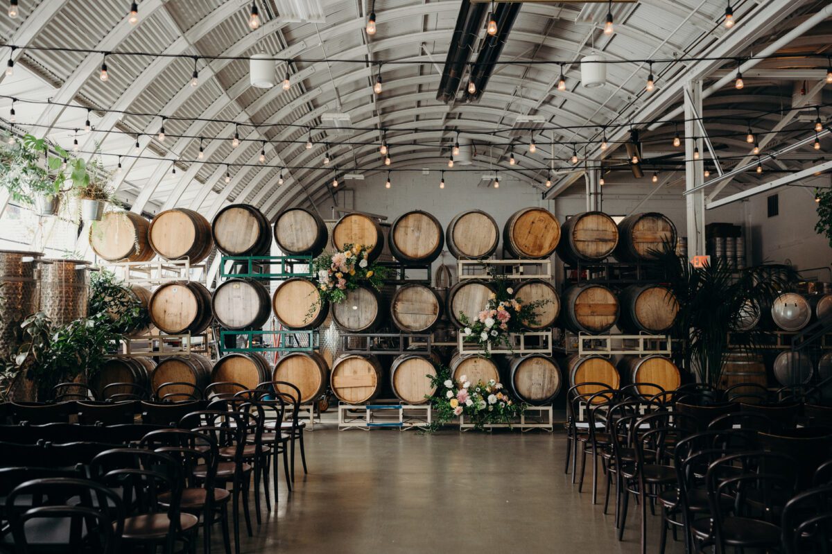 Coopers Hall as a pretty industrial indoor wedding venue set up for a ceremony with flowers on a large stack of wood wine barrels and bent wood chairs lined up for guests.
