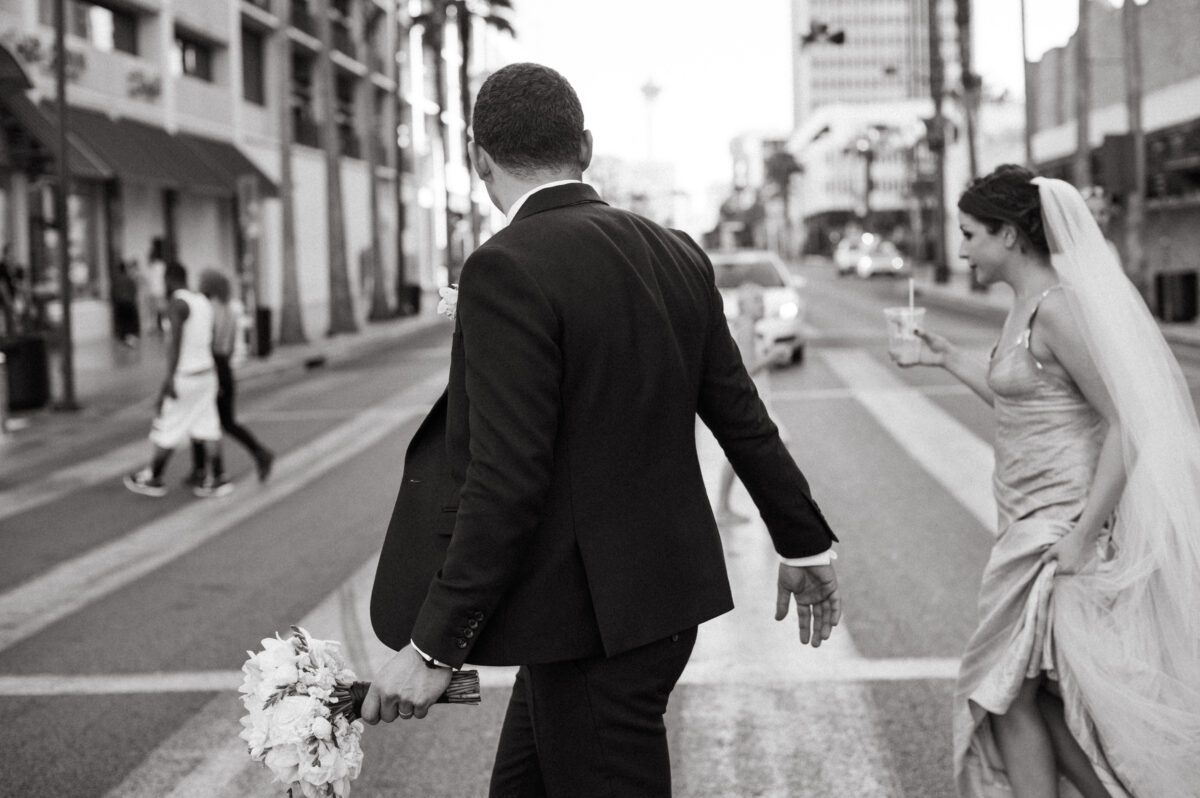 Black and white candid photograph of a newlywed couple in their wedding best crossing a street in Las Vegas