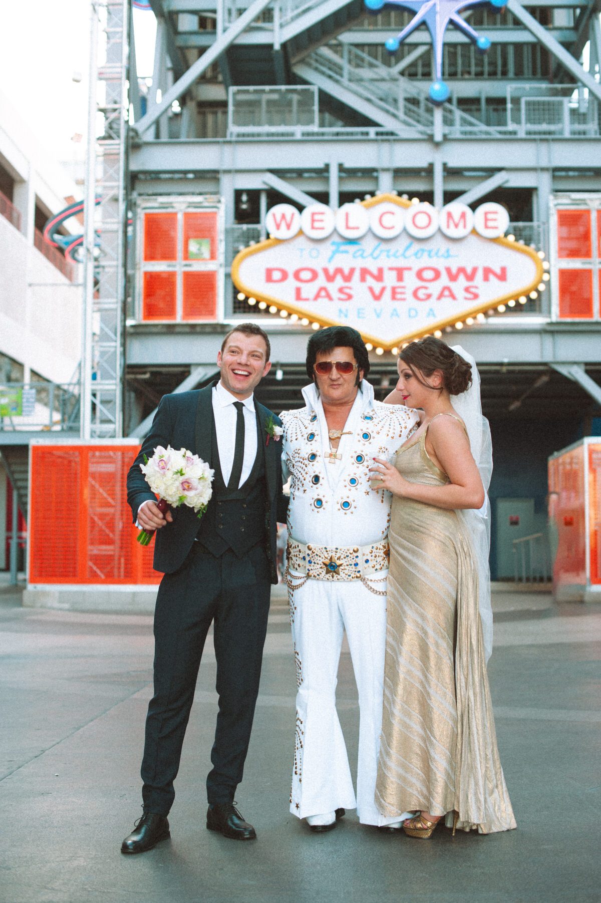 Las Vegas elopement photographer captures a bride and groom posing with an Elvis impersonator in front of the Downtown Las Vegas sign