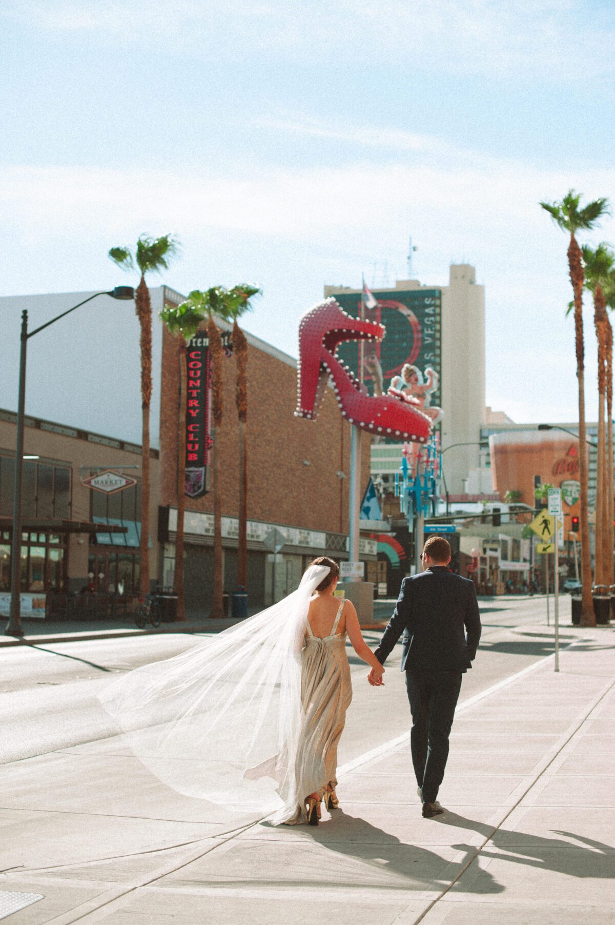Candid portrait of a bride and groom walking away from the camera, veil blowing in the wind. Captured by Las Vegas elopement photographer on a hot sunny summer day.
