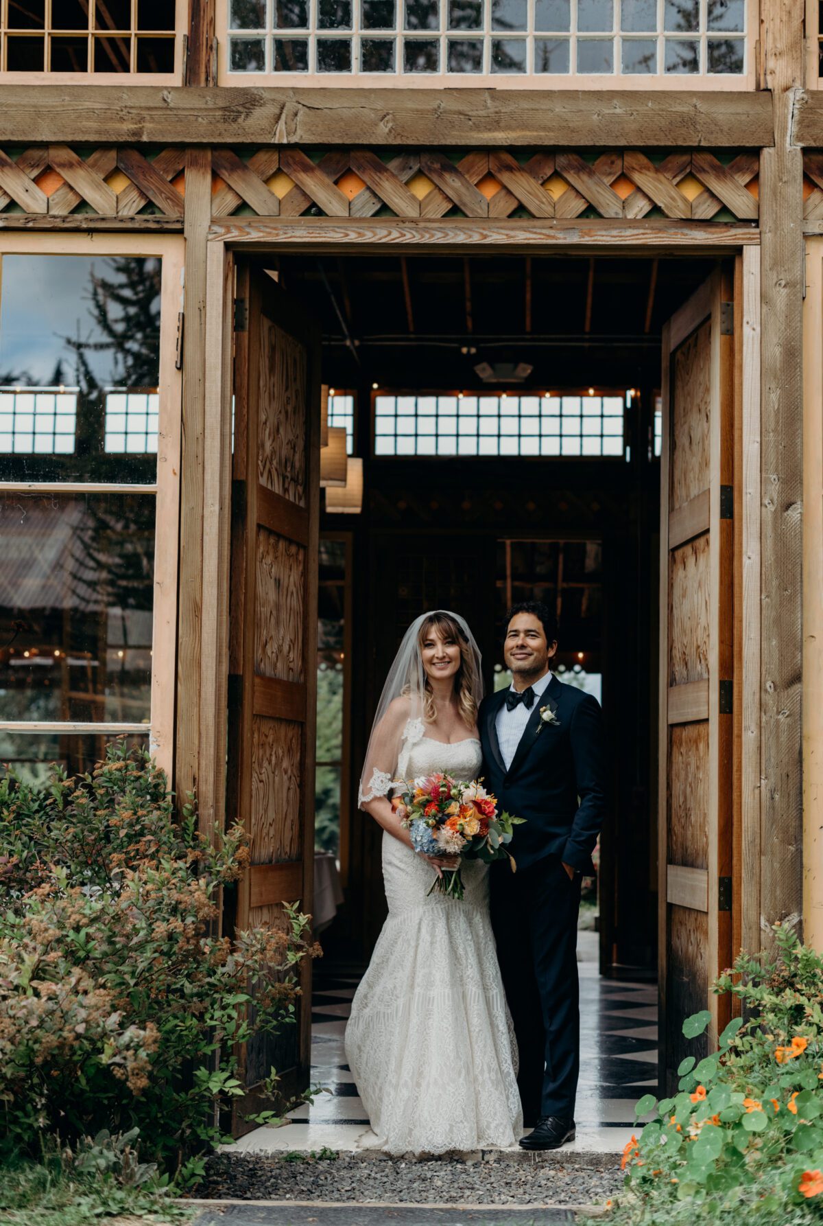 A bride and groom pose at the doors to the indoor event space at mt hood organic farms
