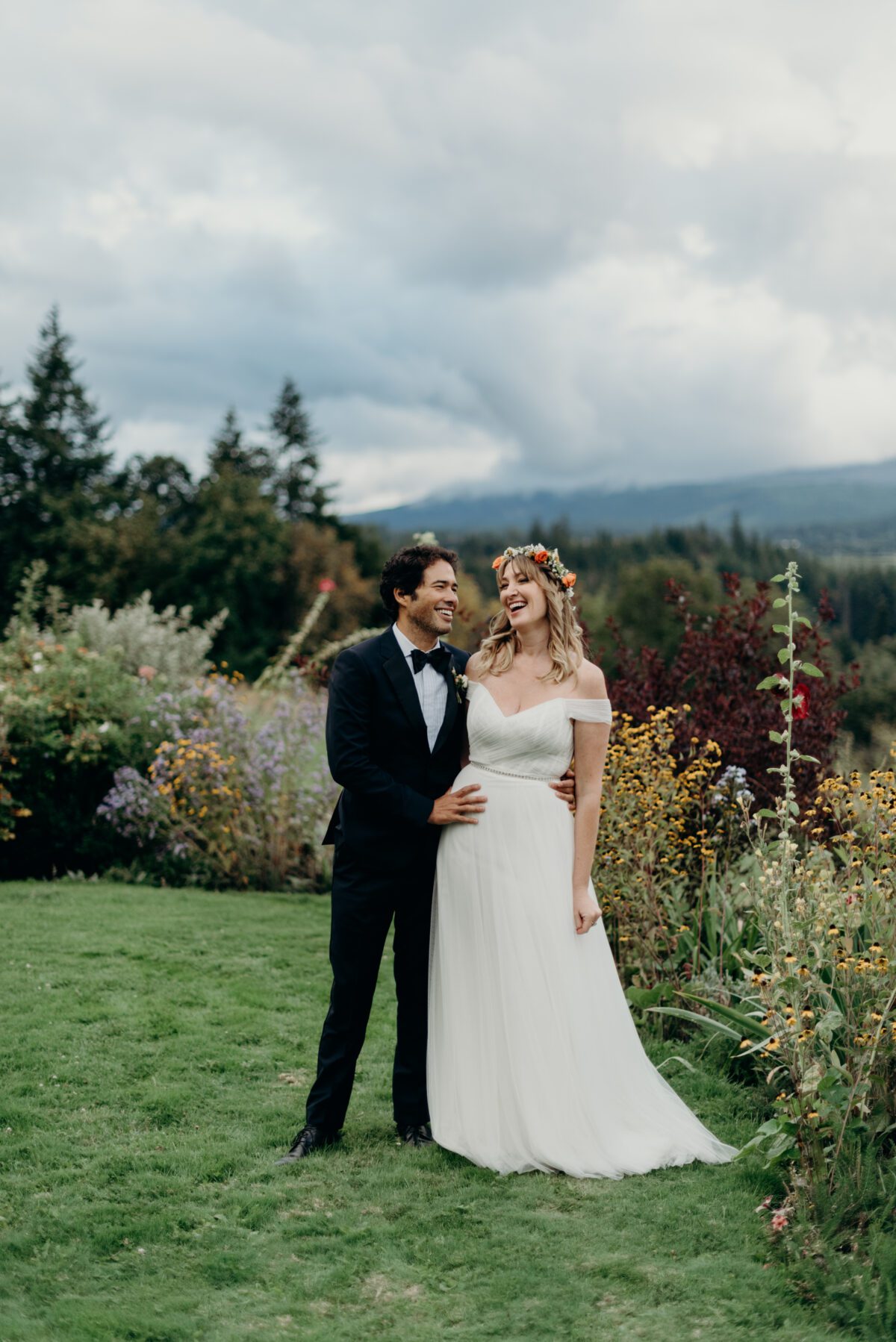 Laughing with joy, a bride and groom stand together beside a flower garden at Mt Hood Organic Farms