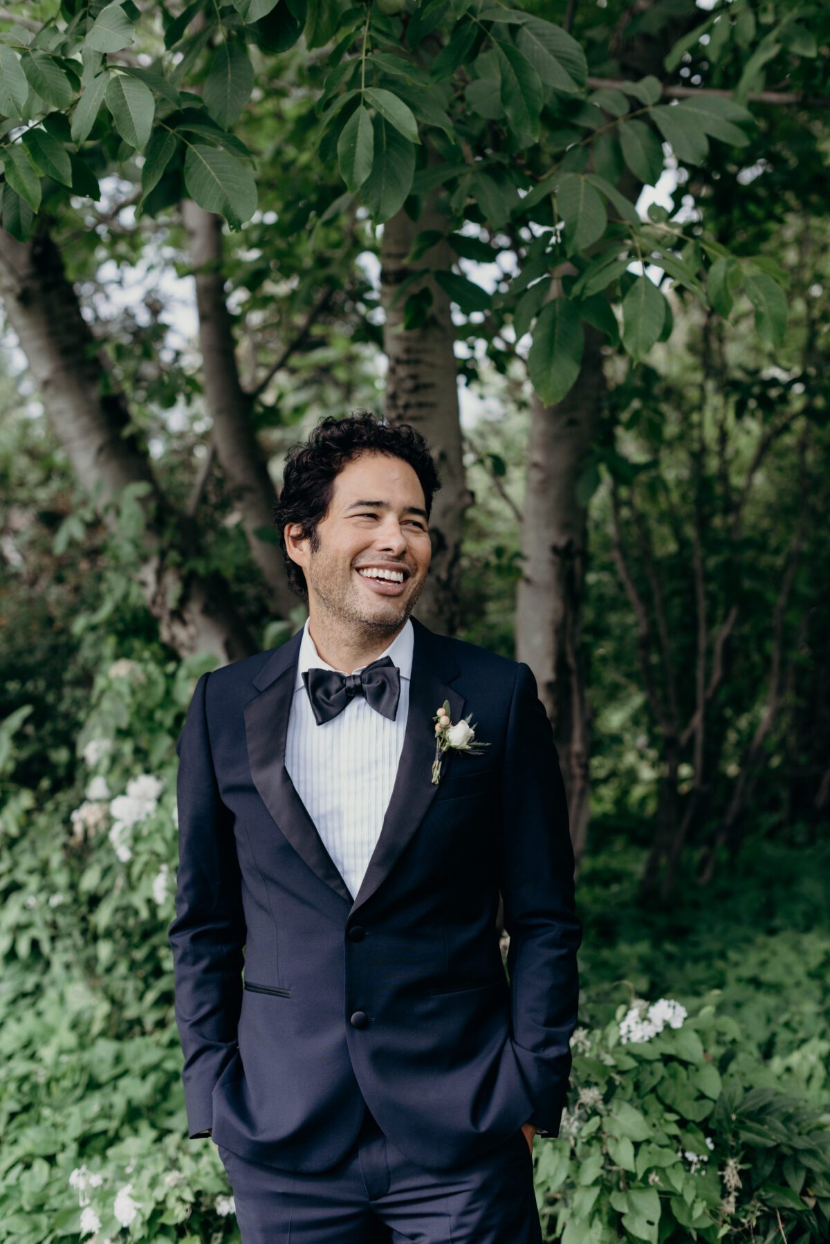 A happy and smiling groom in a black tuxedo poses in front of the garden at mt hood organic farms
