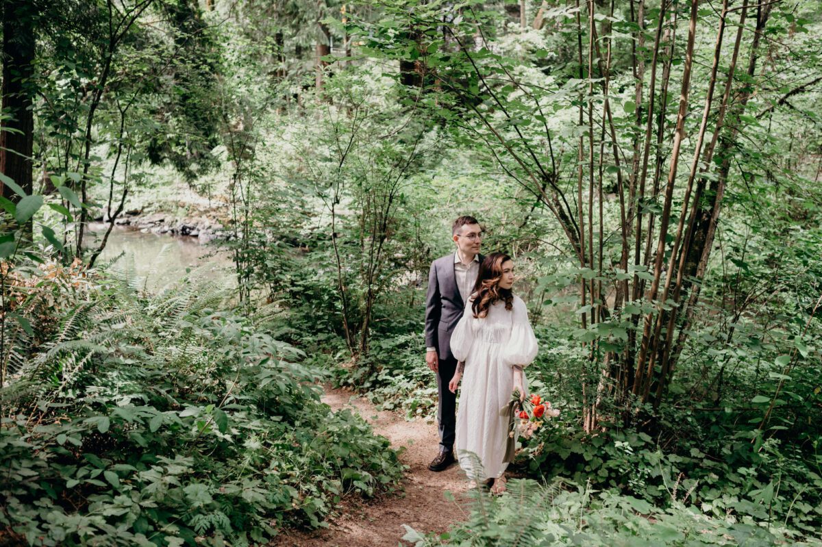 A bride and groom stand in the forest near the creek at their Leach Botanical Garden wedding.