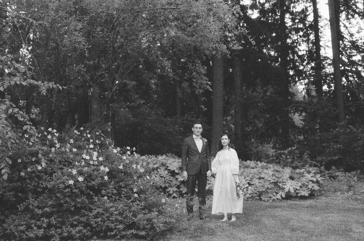 A black and white film portrait of a bride and groom posing in the upper garden at Leach Botanical Garden in Portland, Oregon.
