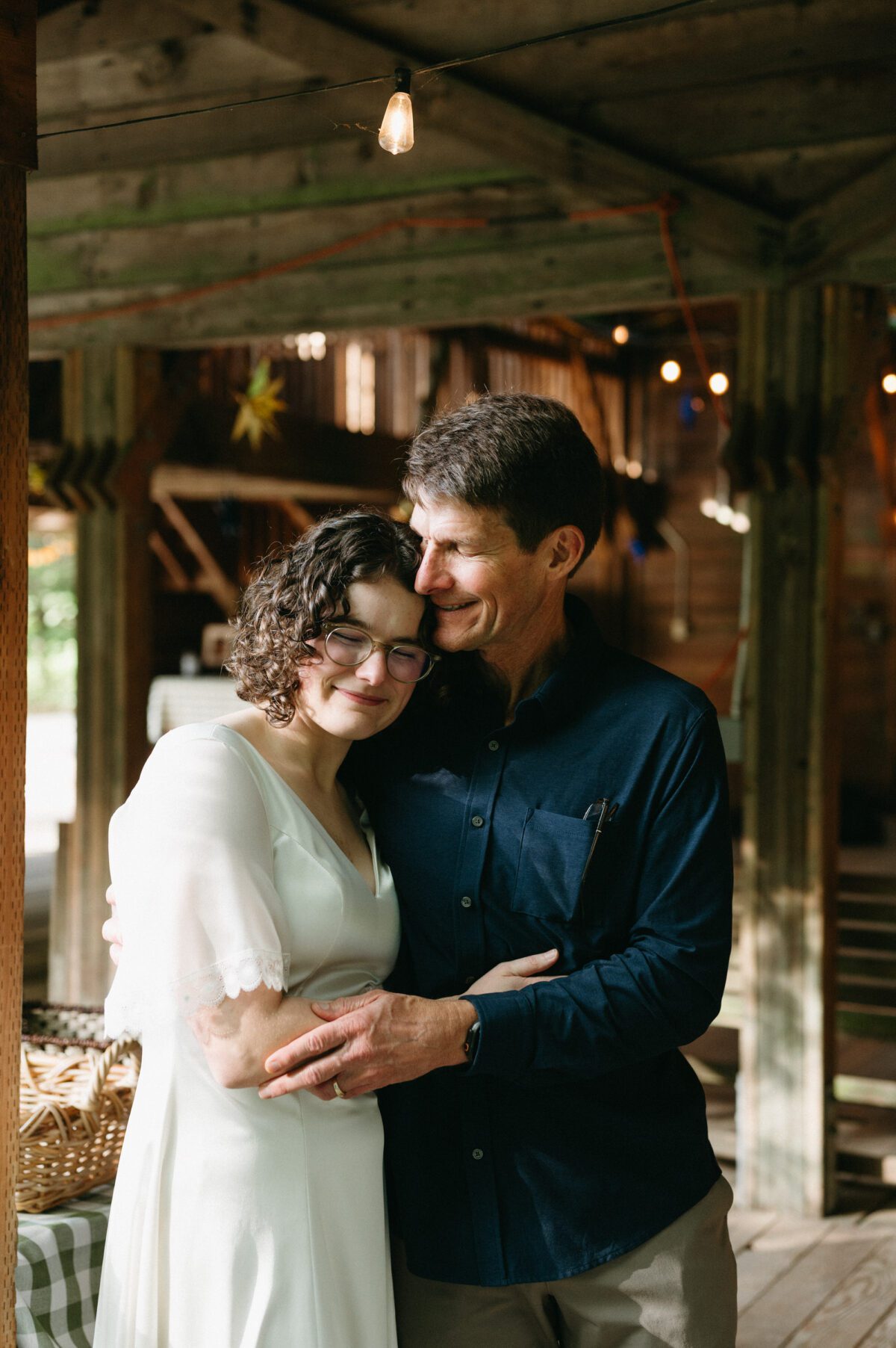 A bride has an unexpected first look with her dad and they hug with faces filled with emotion. Summer camp wedding documentary photography by Briana Morrison