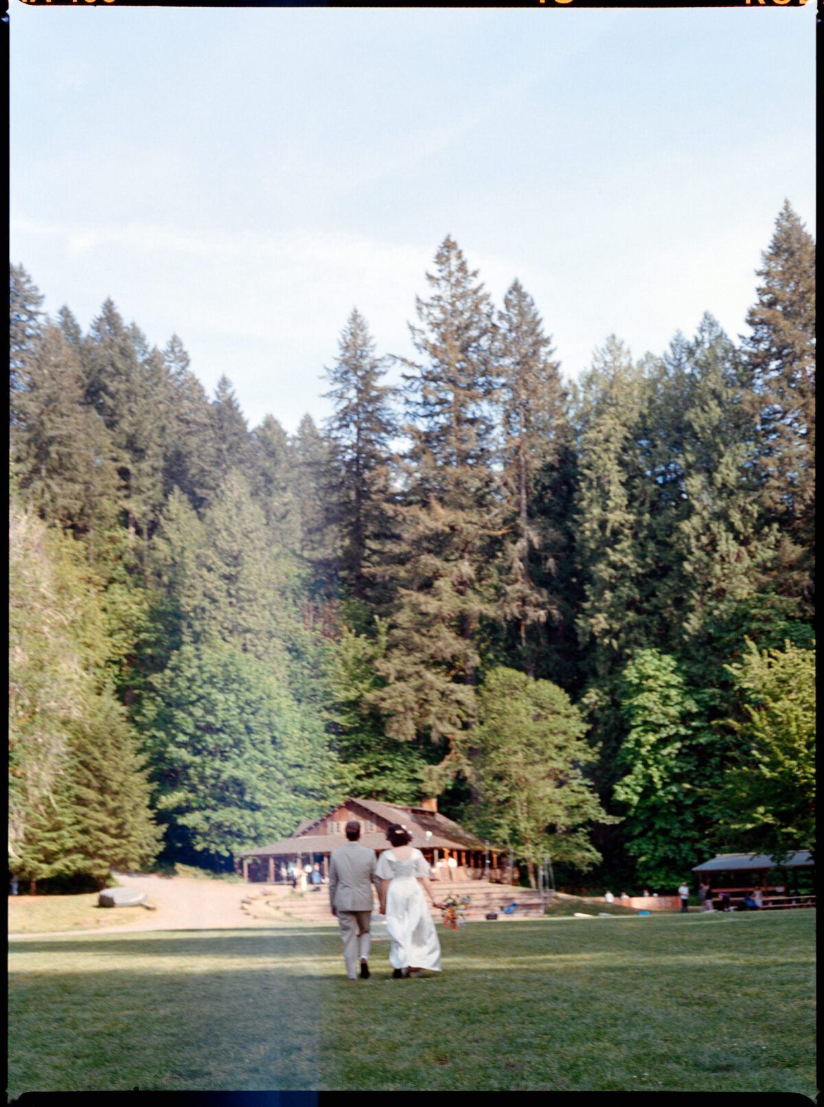 Medium format film photograph of a bride and groom walking towards their wedding celebration at Camp Namanu in Sandy, Oregon. Photography by summer camp wedding photographer Briana Morrison