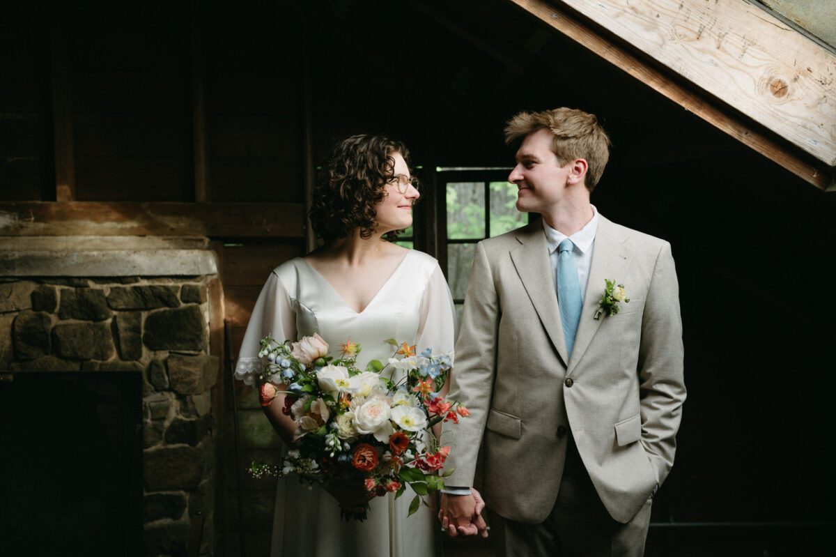 A bride and groom look at each other while standing in window light in the dance hall at Camp Namanu.