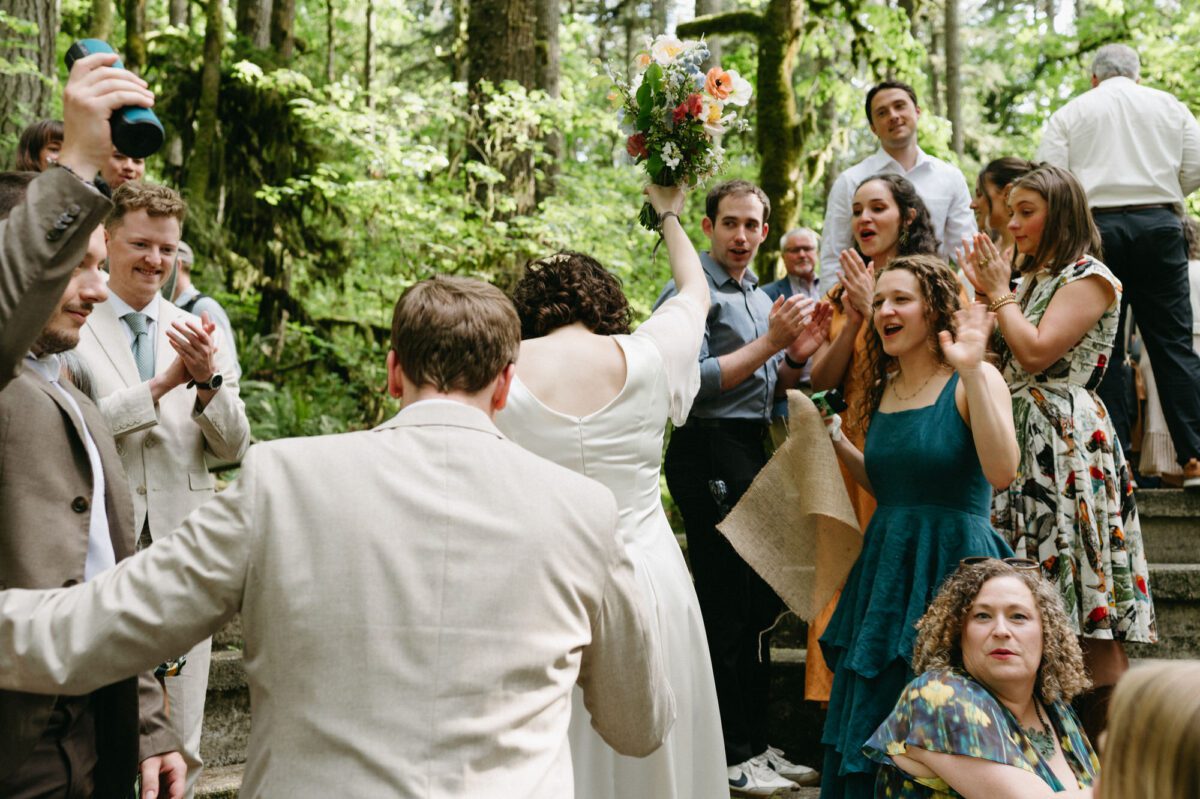The bride and groom lead the way to the wedding meadow while being cheered on by their guests after their summer camp wedding ceremony. Photography by Briana Morrison