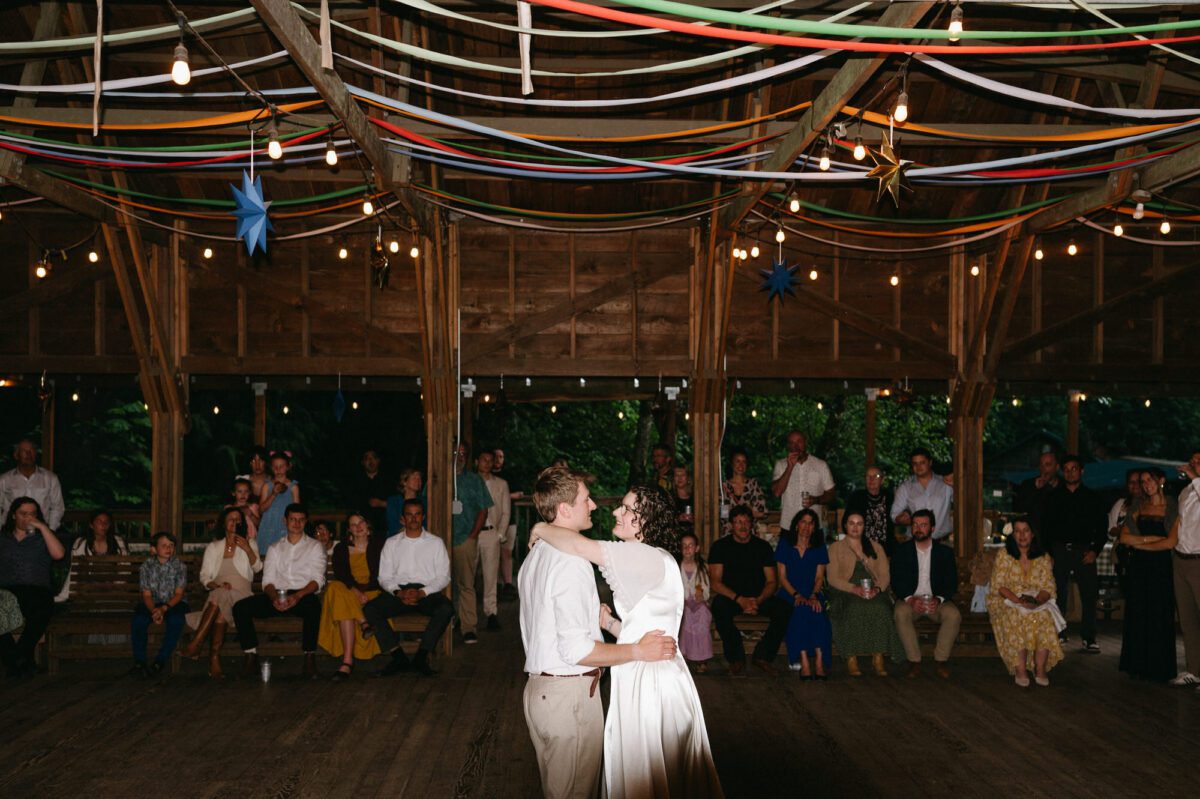 The bride and groom have their first dance under handmade decorations at their Camp Namanu wedding. Photography by Briana Morrison