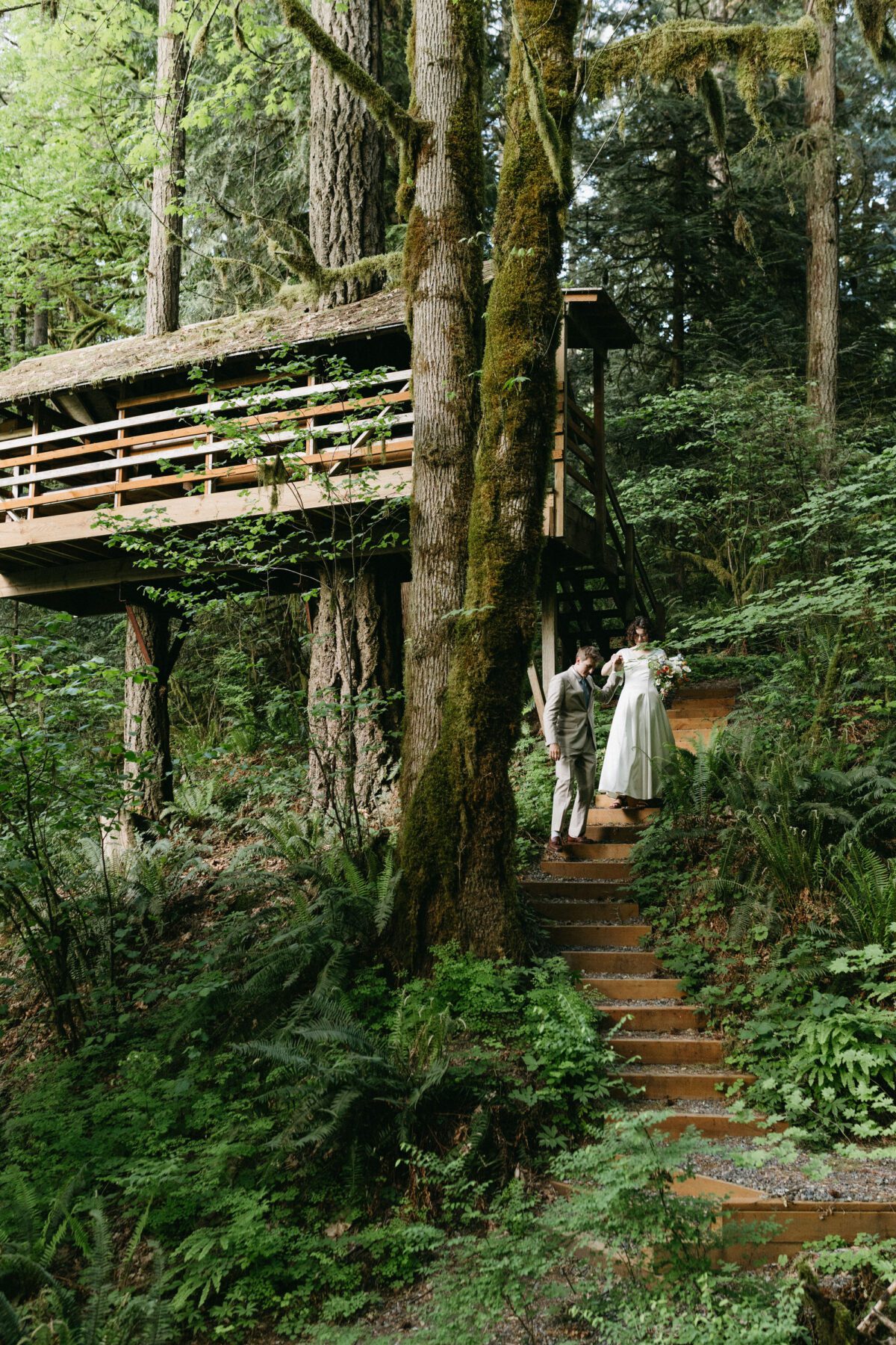 A bride and groom walk down stairs away from a treehouse at Camp Namanu in Sandy, Oregon. Photography by Briana Morrison
